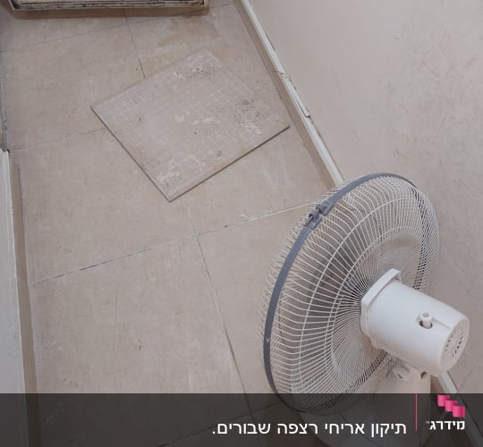 מאוורר עומד על רצפה עם אריחים שבורים